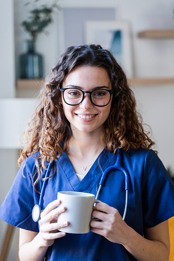 A cheerful nurse with curly hair holding a mug during a break in a medical office