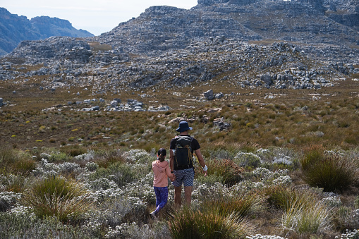 A young girl hikes in the mountains with her dad. They are on a hill with amazing views over the Cederberg Mountains