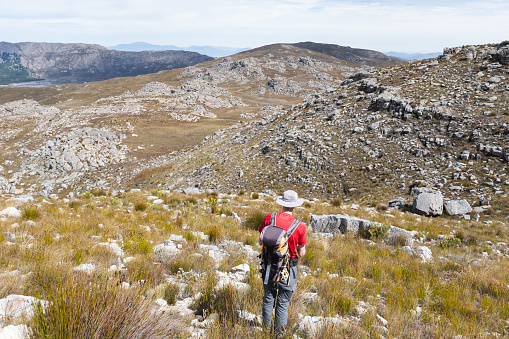 Rear view of a male hiking in the mountains with a large backpack on his back. Vast rocky mountains in the distance ahead of him