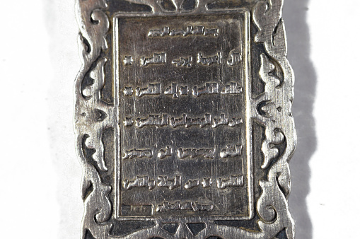 Surah An-Nas in Quran book, Translation (Mankind) on a silver precious metal keyring medal, exchange rate marketing and value, business, price of silver concept, an investment as a store of value, selective focus