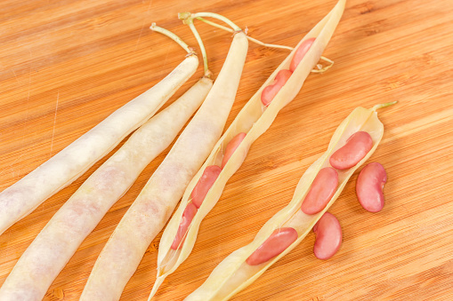 Two open and several whole pods of young red kidney beans lie on the wooden surface, view in selective focus