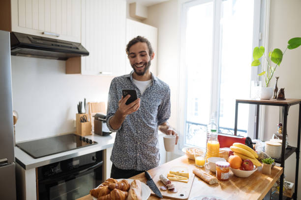 istock Man having breakfast in modern kitchen and using smart phone for business video call 2035094025