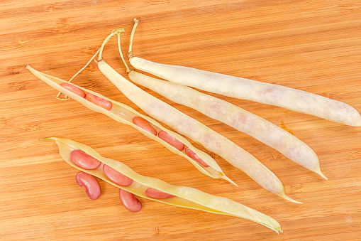 Two open and several whole pods of young red kidney beans lie on the wooden surface, view in selective focus