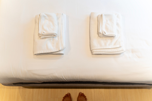 A close-up view of a neatly folded stack of three white towels on a made bed. The towels are different sizes, with the largest one on the bottom and the smallest one on top.