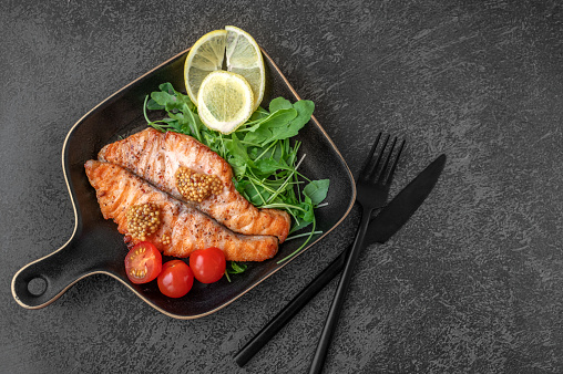 Salmon steak with arugula , lemon and cherry tomatoes in a black grill pan. Top view, copy space.