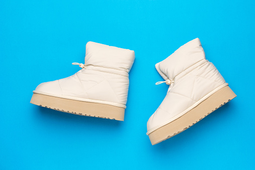 Beautiful beige women's insulated boots on a blue background. Women's shoes for cold weather.