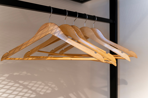 A row of wooden hangers hang neatly on a metal rod inside a closet. Wooden hangers are arranged in a row on a closet rod. The closet is well-organized, with the hangers evenly spaced.