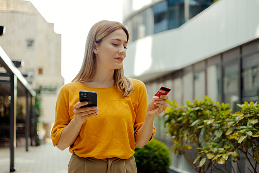 Beautiful woman doing online shopping using credit card through smart phone outdoors