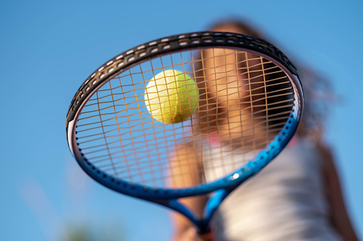 girl is holding a Tennis racket and ball outdoors, blue sky is above her