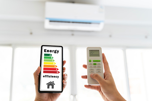 The cell phone is displaying an energy efficiency rating, person is using the remote control to control the air conditioner. Energy efficiency rating on the cell phone is a measure of how efficient.