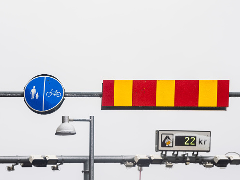 Against a backdrop of overcast skies, a clear indication for pedestrians and cyclists is presented next to a red and yellow barrier, suggesting a restricted area in Gothenburg, Sweden. Below, a streetlight hangs silently, while a price tag showing 22 kr potentially reveals a road toll.