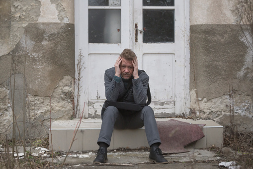 Distraught man sitting in front of ruined abandoned office building