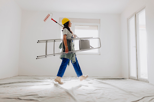 Female worker walking and carrying ladder and paint roller