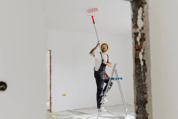istock Handyman with roller on step ladder in room. Ceiling painting 2035248292