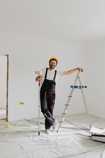 Handyman with roller on step ladder in room. Ceiling painting
