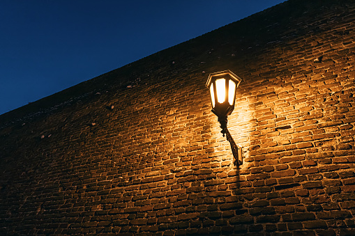 In the dark of night, the flickering light of antique lanterns against the weathered brick walls of fortress creates an enchanting scene of old-world charm.