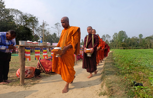 Buddhist monk and Buddhist novice with good spiritual going about with alms bowl to receive food from people a village in Bangladesh.