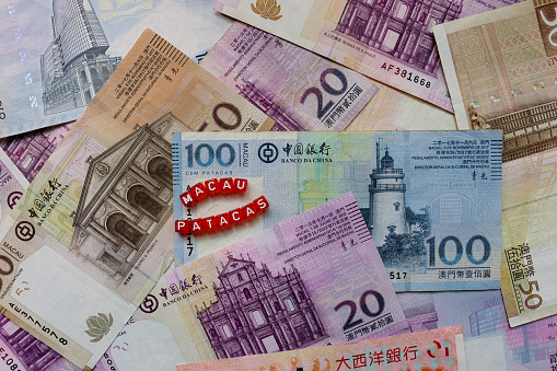 A pile of Macao Money Patacas with a red cubes placed on top, representing foreign currency.
