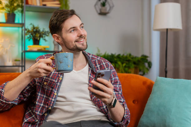istock Happy young man uses smartphone having chat on social media while having hot coffee from cup at home 2035306132