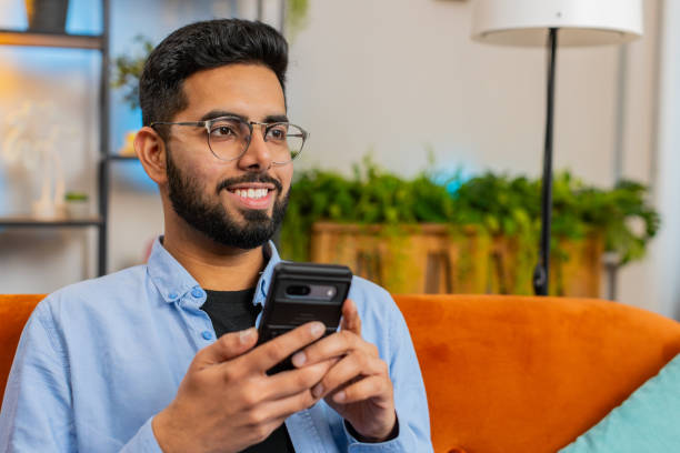 istock Happy Indian man thinking texting messaging on smartphone internet social media app on home sofa 2035323604