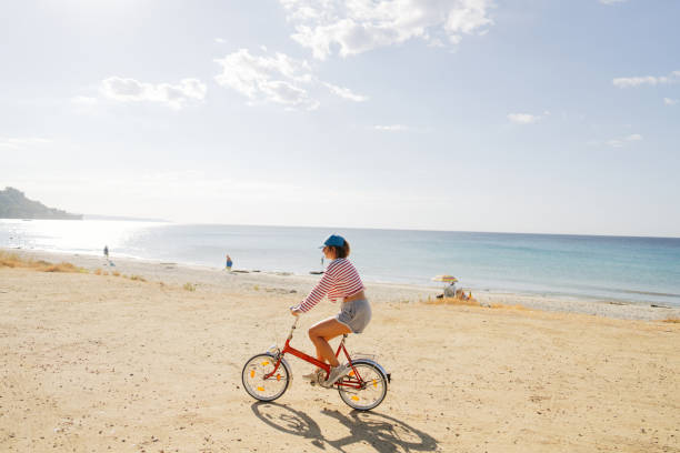 Photo of a young boy and his mom riding along on a bicycle exploring  the coast by the sea