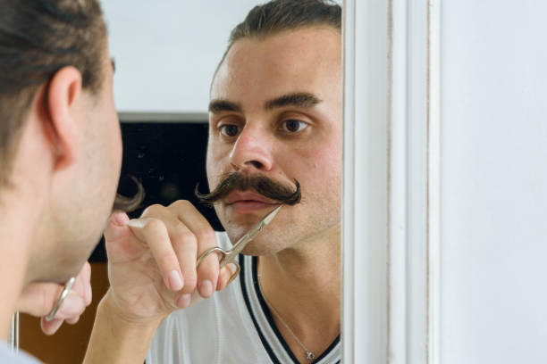 reflection in mirror of non-binary latin person fixing his mustache with scissors - contreras zdjęcia i obrazy z banku zdjęć