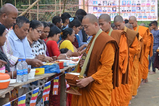 Buddhist monk and Buddhist novice with good spiritual going about with alms bowl to receive food from people a village in Bangladesh.