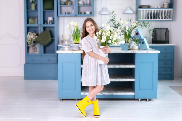 happy little girl with long hair in a white dress and in yellow rubber boots with a bouquet of flowers, stands near kitchen. childhood concept. birthday. mothers day. child is preparing for easter. - single flower flower mothers day easter ストックフォトと画像