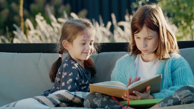 Cute children reading a book, relaxing on a garden swing in the backyard of the house