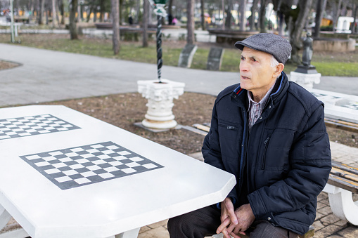 Senior man is waiting for his friends to play chess outdoor in public park.