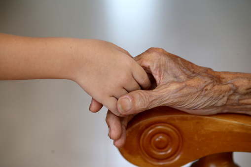 An Asian young boy is holding his grandfather's hand at home