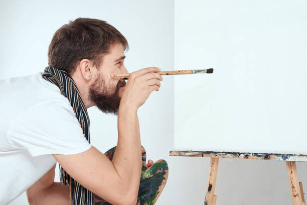 istock Male artist paints on easel palette art creativity light background 2035354408