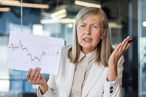 Confused businesswoman analyzing volatile market chart in office. Concept of financial analysis, market fluctuations, and executive concern.