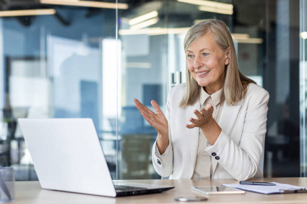 istock Senior female boss smiling talking remotely with colleagues partners, experienced gray-haired businesswoman using laptop for video call, smiling at workplace inside office 2035363145