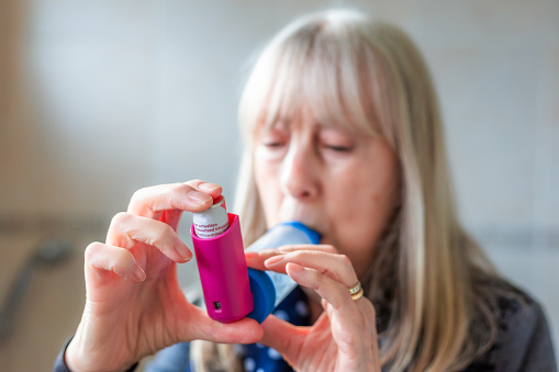 A senior woman using her asthma inhaler while having an asthma attack at home.