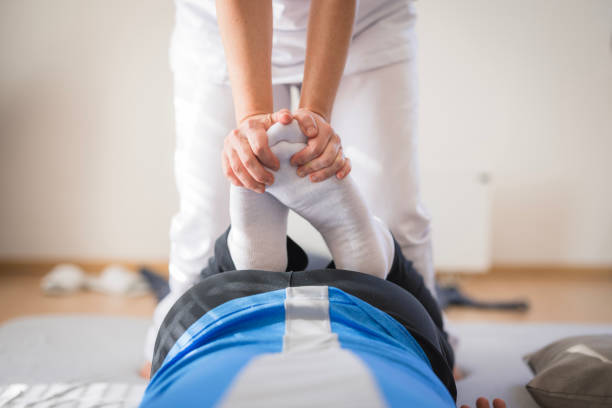 Close up of hands masseur therapist doing wellness leg massage for sporty man, relaxing massaging thigh. Handsome athletic man visit doctor in medical clinic. Rehab massage concept. Copy ad text space