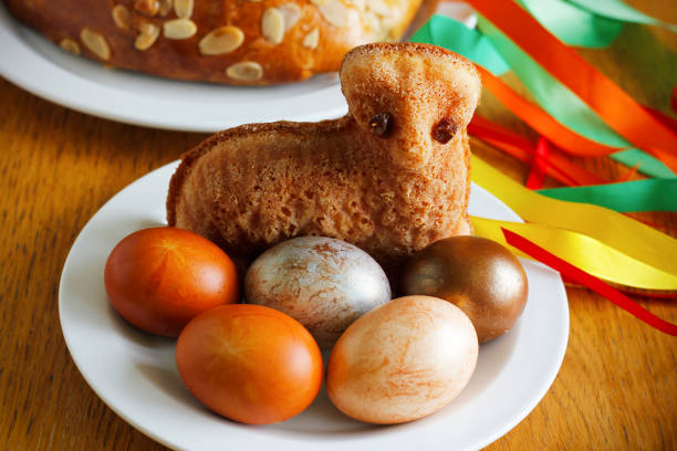 Easter still life containing a small lamb cake, painted eggs, traditional Czech Easter sweet cake called mazanec and an Easter whip with colorful ribbons in the background. Traditional Czech Easter symbols