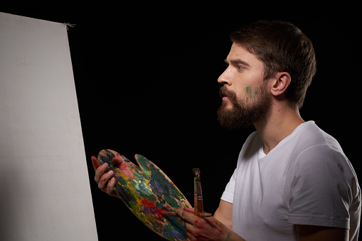 A man with a palette in his hands brush easel art Creative approach hobby dark background. High quality photo
