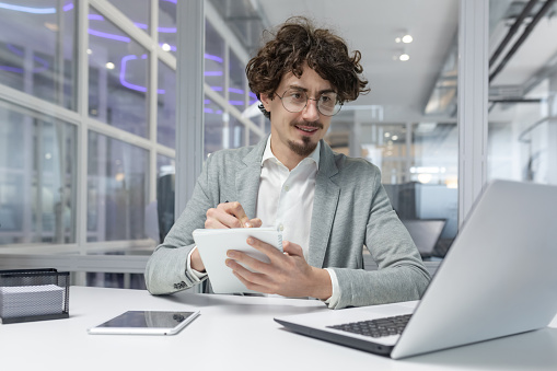Professional young male with curly hair working at laptop in a corporate office setting, showing focus and expertise.