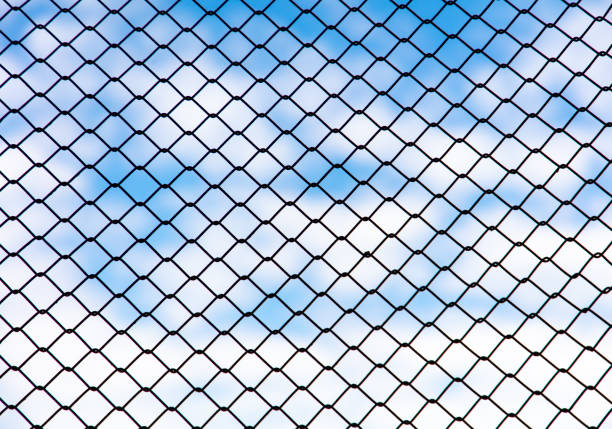 Chain link fence against the blue sky and clouds. Abstract background.