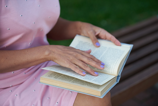 Woman in a pink dress reading a book on a bench outside