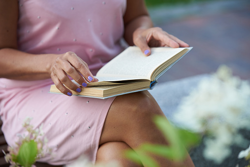 Woman in a pink dress reading a book on a bench outside