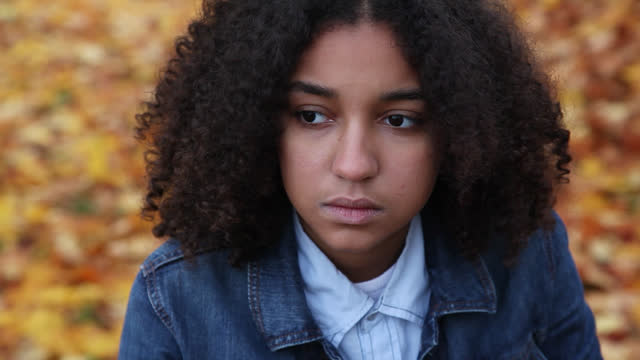 Beautiful biracial African American girl teenager young woman looking sad or depressed wearing a denim jacket outside