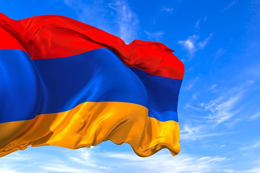 The national flag of Armenia with fabric texture waving in the wind on a blue sky. 3D Illustration