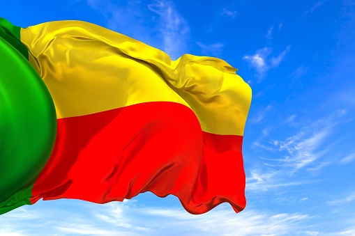 The national flag of Benin with fabric texture waving in the wind on a blue sky. 3D Illustration