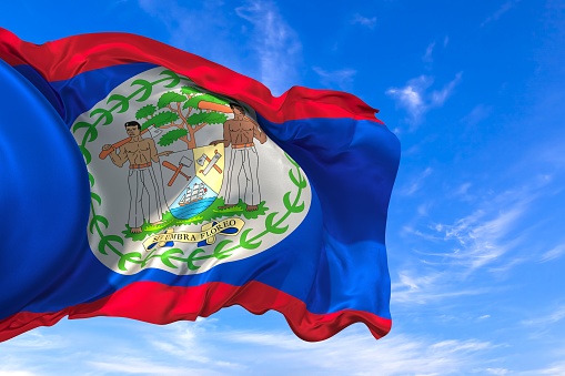 The national flag of Belize with fabric texture waving in the wind on a blue sky. 3D Illustration