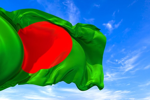 The national flag of Bangladesh with fabric texture waving in the wind on a blue sky. 3D Illustration