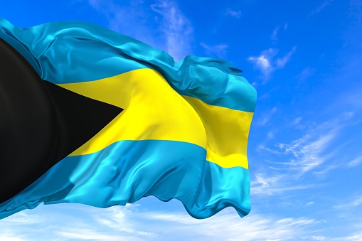 The national flag of Bahamas with fabric texture waving in the wind on a blue sky. 3D Illustration