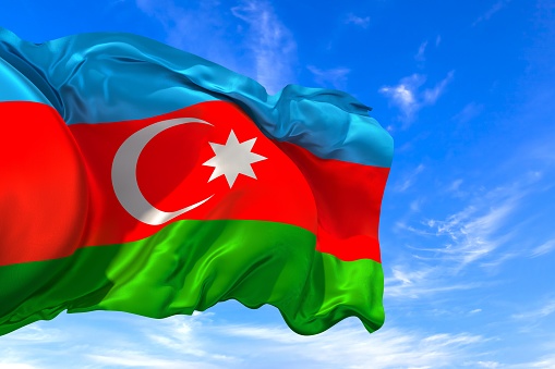 The national flag of Azerbaijan with fabric texture waving in the wind on a blue sky. 3D Illustration