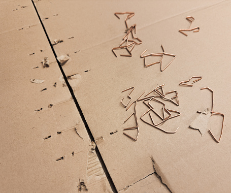 A cardboard box, once closed with metal staples, is now open and the staples are removed and put aside